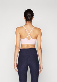 Ανοιχτό ροζ αθλητικό σουτιέν με σχέδιο σταυρωτής πλάτης. Συνδυασμένο με σκούρα μπλε ψηλόμεσα κολάν. Λείος υφασμάτινος χαρακτήρας, ελάχιστες λεπτομέρειες.