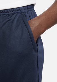 Navy Trackpants mit glatter Textur, elastischem Bund und sichtbaren Seitentaschen. Der Stoff wirkt leicht und flexibel.