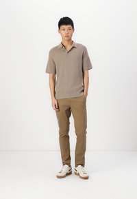 Polo shirt beige avec texture et manches courtes, associé à un pantalon chino marron clair et des baskets arborant un schéma de couleurs blanc et marron.