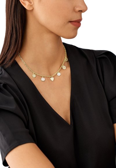 Náhrdelník ve zlaté barvě s řetízkovým designem a pěti pendanty: dva kruhy, jedno srdce a dvě texturované disky. Nesený na černém topu.