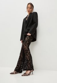 Black blazer over a black lace top and lace pants, featuring a floral pattern. Black and brown leopard print heels complete the look.