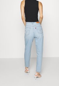 Jeans bleu clair à taille haute avec une jambe fuselée et un léger effet délavé, dotés de poches arrière emblématiques et d'un patch en cuir marron de la marque.