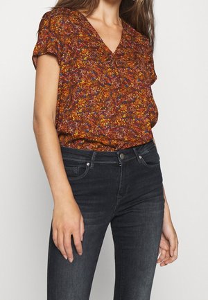 Korte mouwen, v-hals top in een bloemenpatroon met oranje, gele en blauwe tinten, gecombineerd met donkere spijkerbroek. Zacht, lichtgewicht stof.