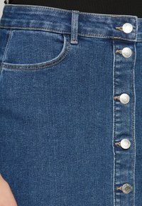 Jeanskjol med en mörkblå tvätt, åtsittande design, framficka och fem silverfärgade metallknappar längs framsidan.