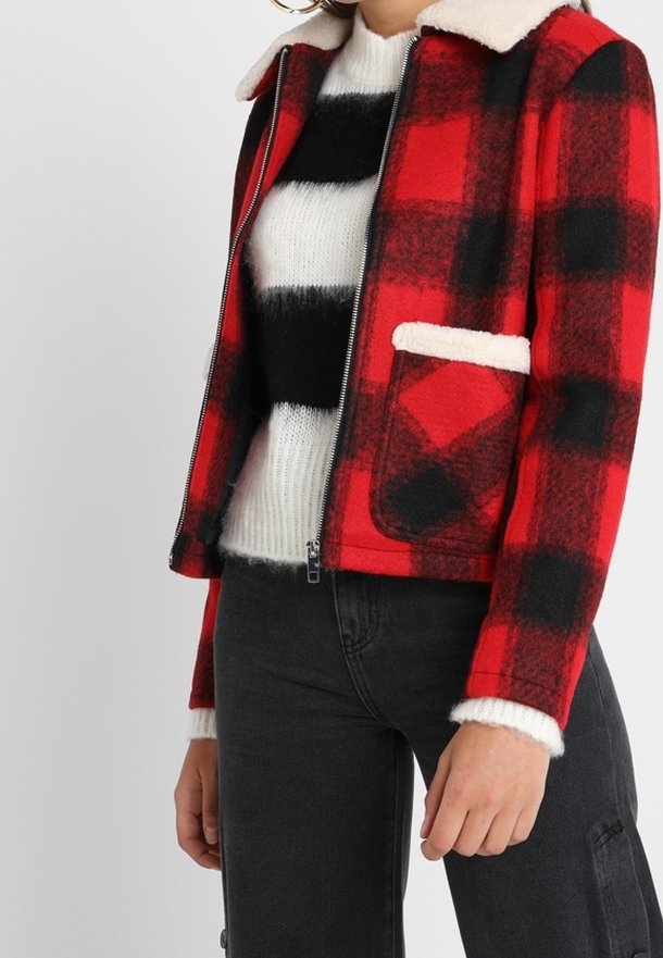 Rød og sort ternet jakke med en cremefarvet imiteret pelskrave og lomme, kombineret med en hvid og sort stribet sweater. Tekstureret stof.