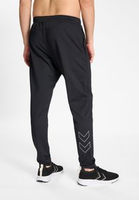 Black athletic joggers with an elastic waistband, side pockets, and white chevron design on the lower leg, made from smooth, lightweight fabric.