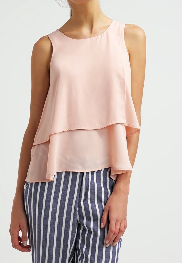 Jasnoróżowa, bezrękawnikowa bluzka z warstwowym wzorem, wykonana z przezroczystego materiału. Połączona z granatowymi i białymi spodniami w paski.