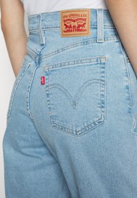Ljust blå denimjeans med hög midja, med en läderpatch för varumärket och en klassisk bakfickdesign med ikonisk sömdetalj.