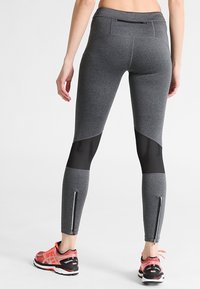 Šedé sportovní legíny s síťovinovými akcenty, přiléhavým střihem, zipovými manžetami a hladkým povrchem. V kombinaci s jasnými běžeckými botami.