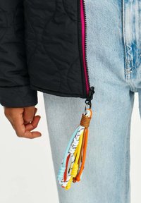 Černá prošívaná bunda s růžovým zipem, spárovaná se světle modrými džíny. Z zipu visí barevná šňůrka.