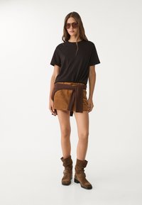 Czarna krótka koszulka z krótkim rękawem w połączeniu z brązową zamszową mini spódnicą z materiałowym paskiem. Brązowe wysokie buty do kolan z zagiętym cholewką.