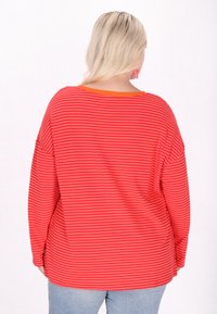 Tricou cu mânecă lungă de culoare roșie, cu dungi orizontale de culoare roz deschis, având un decolteu larg și o croială confortabilă, asortat cu blugi albaștri.