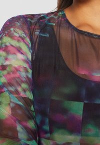 Transparant zwart topje met een meerkleurig abstract patroon in groene, paarse en blauwe tinten; ronde hals, lichtgewicht stof, licht gestructureerd.