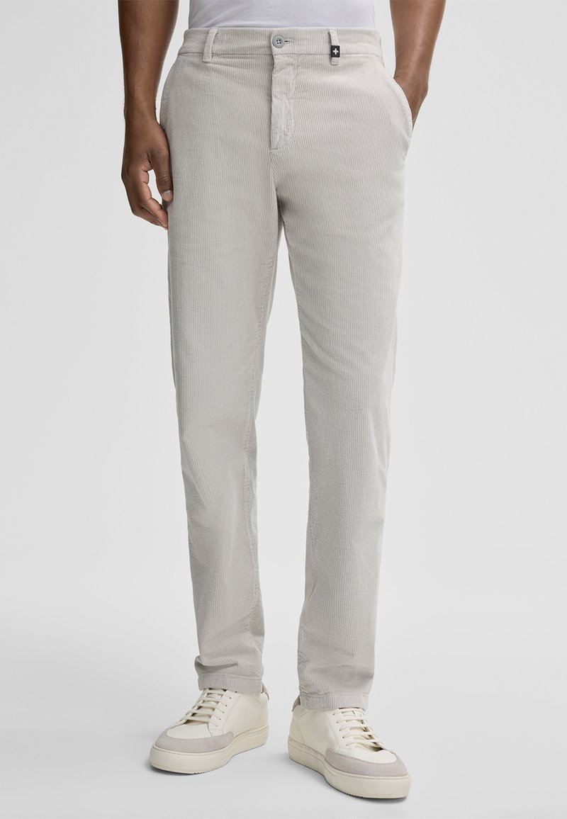 Pantaloni in corduroy grigio chiaro con vestibilità dritta, dotati di chiusura con bottone, tasche laterali e superficie strutturata. Abbinati a sneakers bianche.