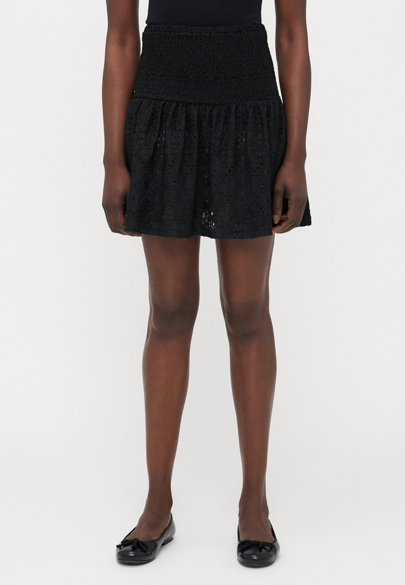 Zwarte rok met een geplooid tailleband, gelaagd ontwerp en bloemenoog patroond. Zachte textuur, knie-lang, gecombineerd met zwarte ballet flats.