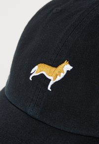 Sort baseballkasket med et struktureret stof. Har en broderet gul og hvid hundesilhuet på fronten.