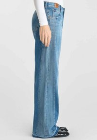 Lichtblauwe wijde spijkerbroek van denim, met een hoge taille, subtiele vervaging en een leren merkpatch op de achterkant van de taille.