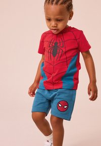 Rød og blåt Spider-Man inspireret t-shirt med sort edderkop grafik, kombineret med blå shorts med en edderkop-logo. Glat bomuldsstof.