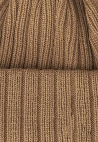 Berretto di maglia marrone chiaro, con una texture a coste e un risvolto piegato. Il materiale appare morbido e caldo, adatto per il freddo.