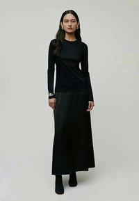 Top preto de manga longa combinado com uma saia preta fluida, ambos feitos de tecidos suaves. O conjunto apresenta um design minimalista com uma silhueta elegante.