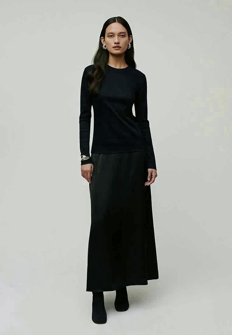 Un haut à manches longues noir associé à une jupe fluide noire, tous deux en tissus lisses. La tenue présente un design minimaliste avec une silhouette épurée.