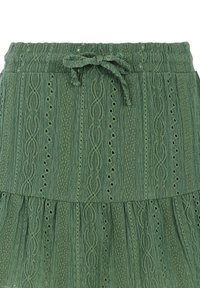 Falda verde en capas hecha de tela texturizada. Cuenta con una cintura ajustable con cordón y ojales decorativos, además de intrincados patrones tejidos.
