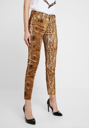 Slim-fit brune og sorte bukser med slangeprint, båret med sorte højhælede sko og en hvid top, vist fra talje til fødder.