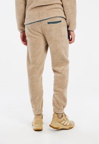 Pantalones de chándal de forro polar beige con puños elásticos, que cuentan con un bolsillo trasero y una superficie texturizada. Combinados con zapatillas beige.