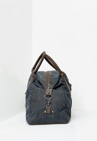 Torba sportowa z płótna w ciemnoszarym kolorze, z brązowymi skórzanymi akcentami, podwójnymi uchwytami u góry oraz zapięciem na zamek błyskawiczny z metalowymi detalami.