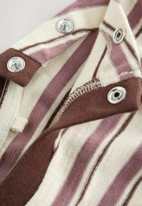 Záběr zblízka na látku s vodorovnými pruhy v barvách krémová, fialová a hnědá s stříbrnými patentními knoflíky a viditelnými švy.