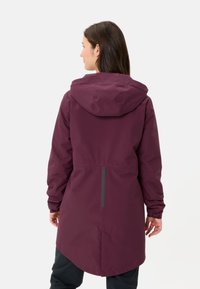 Giacca impermeabile color bordeaux con cappuccio, maniche lunghe, polsini elasticizzati e orlo asimmetrico. Include un accento riflettente sul retro.