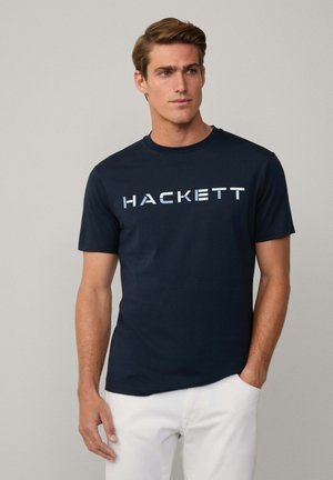 Camiseta de algodón azul marino de manga corta, con la palabra "HACKETT" en letras blancas negrita en el pecho. Cuello redondo estándar.