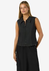 Ärmlös svart denimtop med dragkedja fram, bred krage och orangea sömnadsdetaljer. Figurformad design. Matchas med lösa svarta byxor.