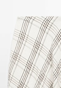 Tissu blanc avec un motif à carreaux composé de fines lignes noires et brunes qui se croisent pour former des carrés.
