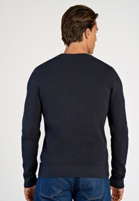 Navyblauer, gerippter Strickpullover mit langen Ärmeln und rundem Ausschnitt. Verfügt über einen Saum, der auf der Taille sitzt, kombiniert mit Jeans.
