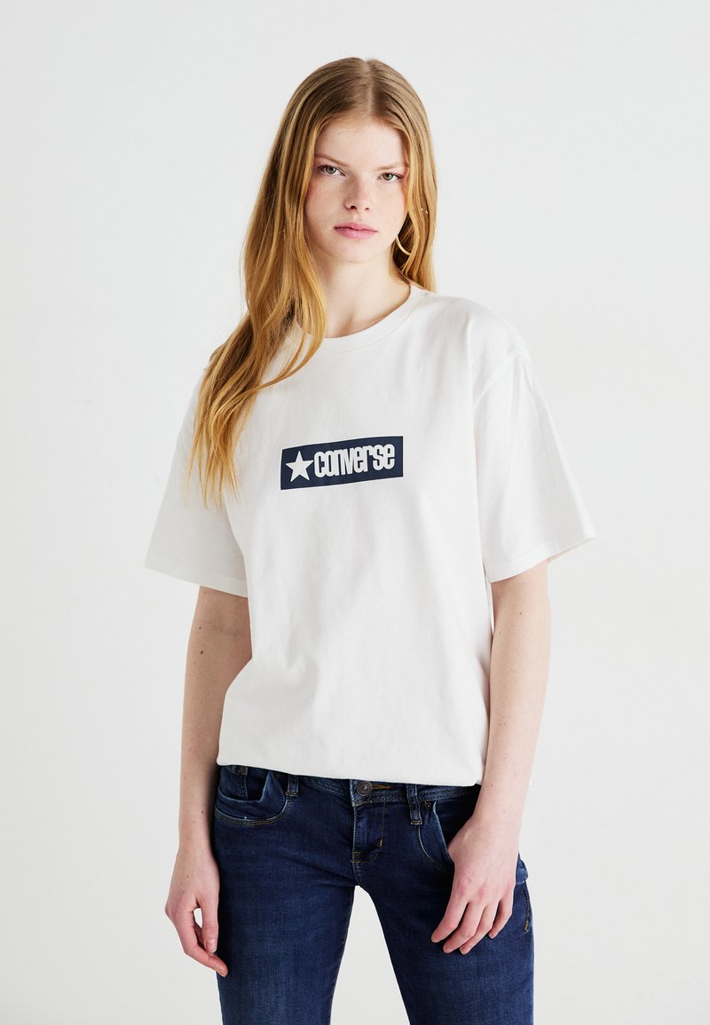 Weißes Baumwoll-T-Shirt mit einem navyblauen rechteckigen Grafik, auf der das Wort "Converse" und ein Stern abgebildet sind. Kurze Ärmel, lässige Passform.