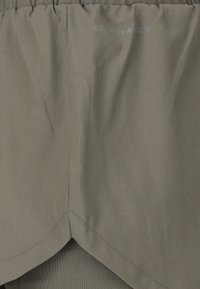 Olivengroen stof met elastische tailleband en "Endurance" gedrukt vlak bij de bovenkant, met een gebogen zoomdetail aan de onderkant.