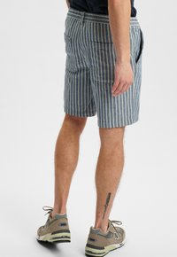 Gestreepte shorts van blauw en crèmekleurige stof, met zakken en een relaxte pasvorm. Gecombineerd met neutraal gekleurde sportschoenen.