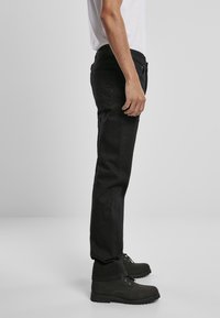 Crne traperice s ravnim krojem, s pet džepova i suptilnim šavovima. Uparene s crnim suknama.