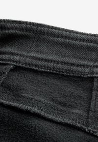 Crni denimski materijal s debeljem, teksturiranom površinom, s vidljivim šavovima duž pojasa i mekim unutarnjim oblogom.