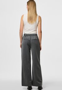 Pantaloni grigi a gamba larga realizzati in tessuto texturizzato. Presentano una cintura elastica e due tasche posteriori. Abbinati a una canotta bianca.