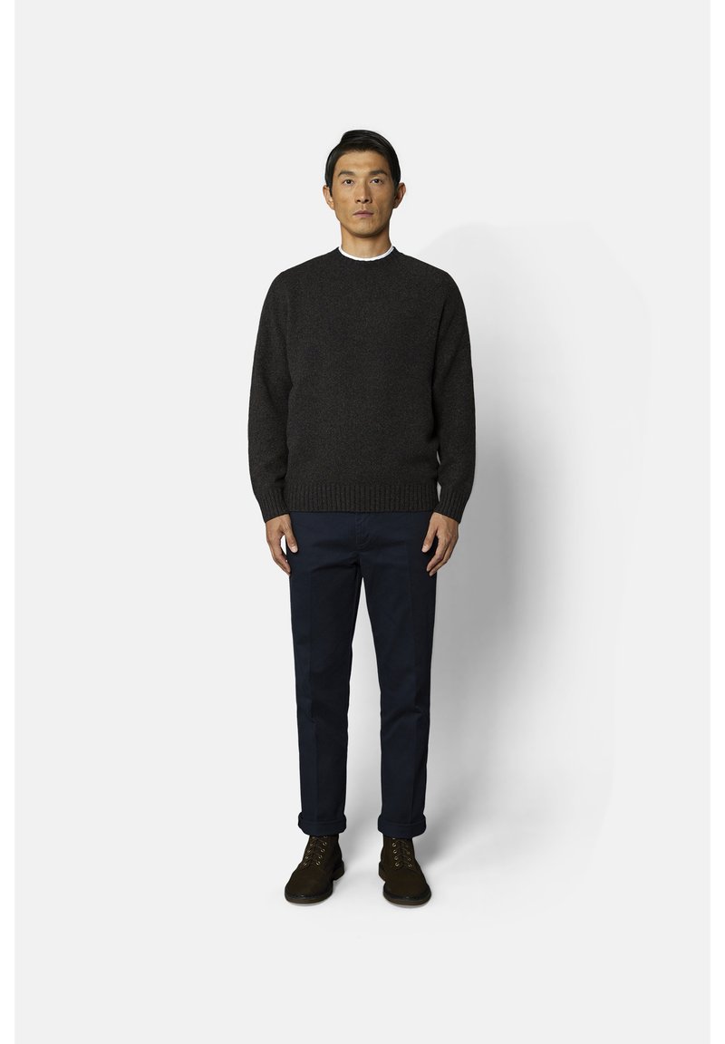 Pull en tricot gris foncé avec col rond, associé à un pantalon bleu marine et des bottes marron à lacets, présenté sur un fond uni.