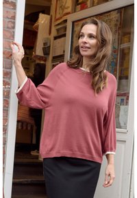 Rose-colored oversized sweater with ¾ sleeves, paired with a black skirt. Soft texture, casual design, and a white collar detail.