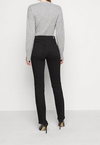 Jeans negros de cintura alta y silueta ajustada, combinados con un suéter gris claro. Los jeans tienen bolsillos traseros y costuras visibles.