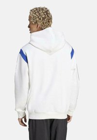 Haut à capuche blanc avec des accents bleus sur les épaules, manches longues et cordon de serrage. Fabriqué en tissu doux avec une coupe décontractée et des poignets côtelés.
