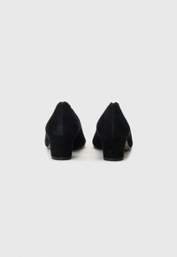 Black suede heeled shoes with a rounded toe and a medium block heel, featuring a smooth texture and seamless construction.