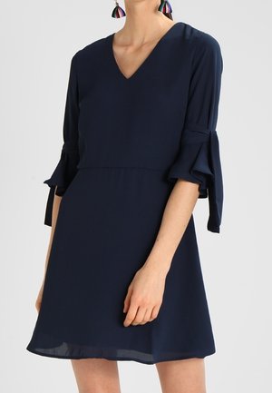 Abito blu navy con scollatura a V, fluido, maniche a tre quarti con dettagli annodati e vita aderente. Tessuto liscio con una leggera trama.