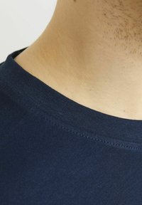 Tamsiai mėlynas medvilninis marškinėliai su apvaliu iškirptu kraštu, švelni tekstūra ir tvarkingais siūlais aplink apykaklę bei peties siūlę.