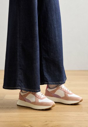 Pink and white sneakers with suede accents, patterned overlays, and a light sole, paired with wide dark denim pants.