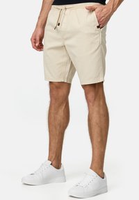 Beige bomuldsshorts med elastisk talje, snor og sidelommer. Sammen med hvide sneakers, der fremhæver en afslappet stil.
